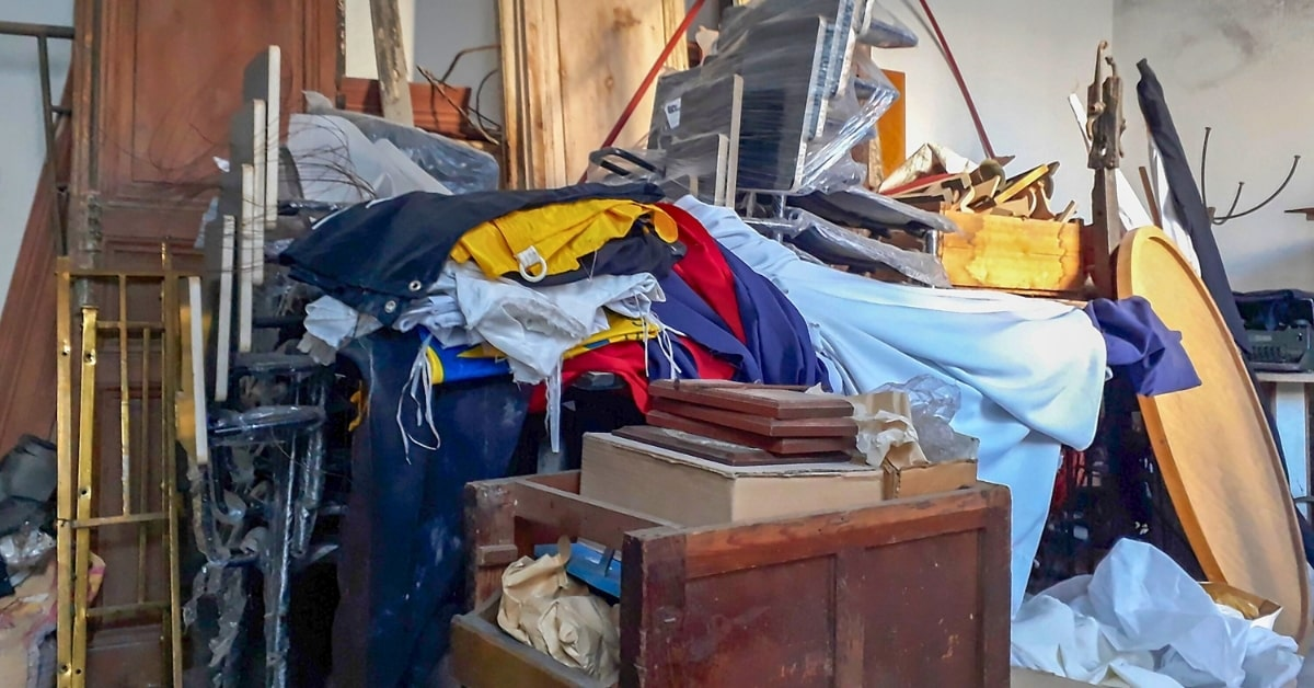 Cluttered interior filled with old clothes, furniture, and miscellaneous junk before a property cleanout in Oklahoma City.