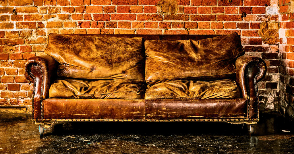 Worn-out brown leather couch against a brick wall ready for removal in Oklahoma City.