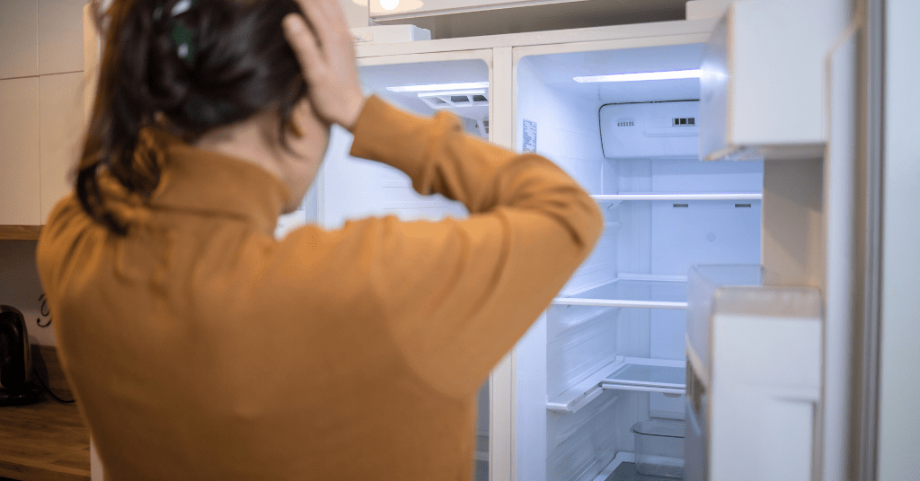 Frustrated woman looking at an empty broken refrigerator in need of removal in Oklahoma City.